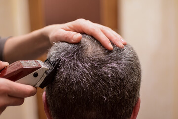 A man is trimmed with a hair clipper and sits with his back to the camera. Perhaps at home in a lockdown