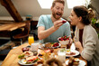 © Drazen - Happy man feeding his girlfriend with strawberries during breakfast at dining table.