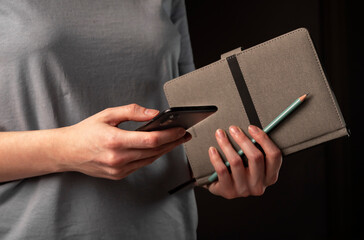 Poster - Female hands holding phone and making appointments, holding planner. Student using smartphone and notebook at night