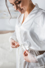 Poster - young bride tying white satin robe in bedroom.