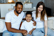© Kanstantsinzzz - Loving black family relaxing at sofa in the morning, happy mixed race parents laughing cuddling having fun with cute little kid child son playing enjoying moments together. High quality photo