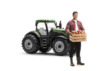 Poster - Full length portrait of a young farmer holding a crate full of fresh apples in front of a tractor