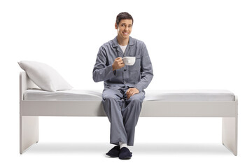 Canvas Print - Young man in pajamas sitting on a bed and holding a cup of tea