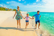 Family at the beach, mother, father and daughter playing, running on the shore, dressed in colorful tropical outfits