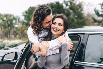 Cheerful young couple hugging near their car, girl smiling, happy girl and man