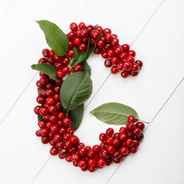 Letter G from summer harvest of cherry on white wooden background. Fruit summer alphabet. Sweet mood font. Letter G from green leaves and cherry berries. Colorful ABC, Text