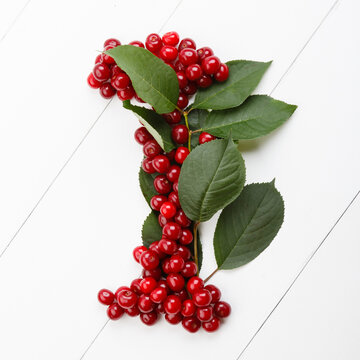 Letter I from summer harvest of cherry on white wooden background. Fruit summer alphabet. Sweet mood font. Letter i from green leaves and cherry berries. Colorful ABC, Text