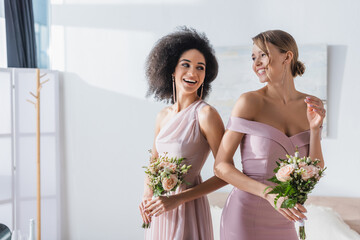 Poster - joyful multicultural bridesmaids holding wedding bouquets in bedroom.