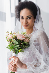 Poster - pretty african american bride holding wedding bouquet while looking at camera.