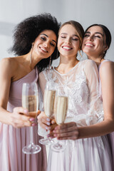 Wall Mural - cheerful bride with bridesmaids clinking champagne glasses on blurred foreground.