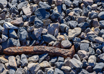 Weathered rusty railroad spike laying among gravel rocks