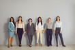 Women business team, cooperation, working in office. Team of young positive businesswomen corporate partners employees standing and holding hands together looking at camera over grey wall background