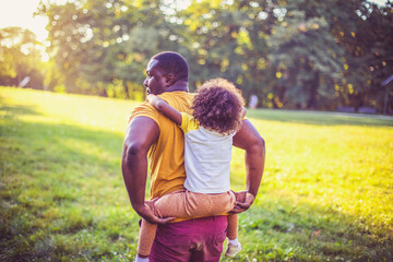 Wall Mural - Father carrying daughter piggyback. African American father and daughter having fun outdoors.