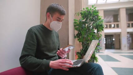 Fototapete - A man in a mask uses a laptop in his hands. He is talking on the phone. Freelancer communication in the workflow.