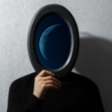 Half Moon Inside Of Mirror Black Frame In Hands Of Man On Textured Grey Background. Contemporary Artwork Collage Concept.