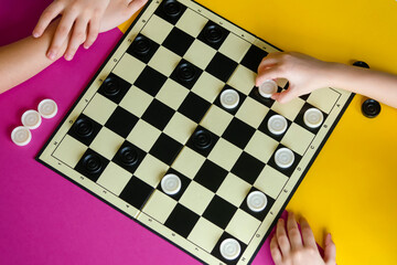 Children play checkers on a colorful table. Boy and a girl compete in board games. Top view.