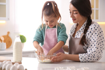 Wall Mural - Mother and daughter making dough at table in kitchen