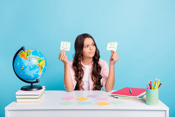 Canvas Print - Portrait of clever school person sitting behind desk look sticker good bad emotes isolated on blue color background