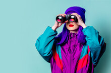 Stylish White Girl With Purple Hair And 80s Tracksuit Using Binoculars On Blue Background