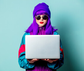 Wall Mural - Stylish white girl with purple hair and 80s tracksuit with laptop on blue background