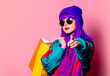 Stylish shopaholic girl in 80s tracksuit and sunglasses hold shopping bags