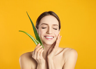 Wall Mural - Happy young woman with aloe leaves on yellow background