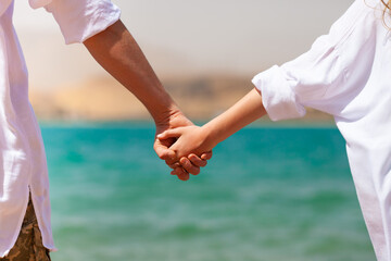 Male and female hands holding close up on background of the blue Red sea and mountains. Travel, tourism, relationship and happiness concept. Back view.