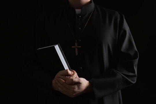Priest with Bible on dark background, closeup
