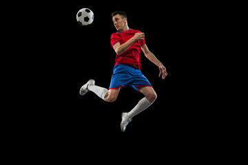 Young Caucasian soccer football player practicing isolated on black background.