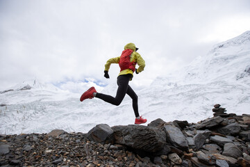 Woman trail runner cross country running up hill to winter snow mountain top