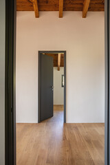 Detail of an open door, empty white room with exposed wood beams and hardwood floors