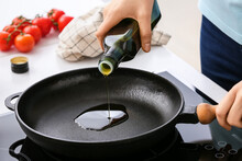 Woman pouring olive oil onto frying pan in kitchen