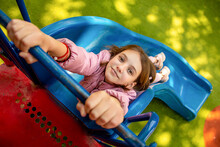 Cute Happy Beautiful Natural Teenage Girl In A Pink Jacket Is On A Playground With A Green Special Coating Hanging On A Slide On A Sunny Day