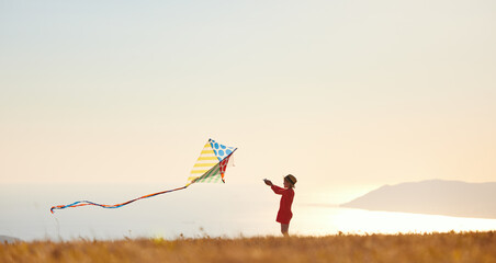 Poster - happy child girl launches a kite at sunset outdoors