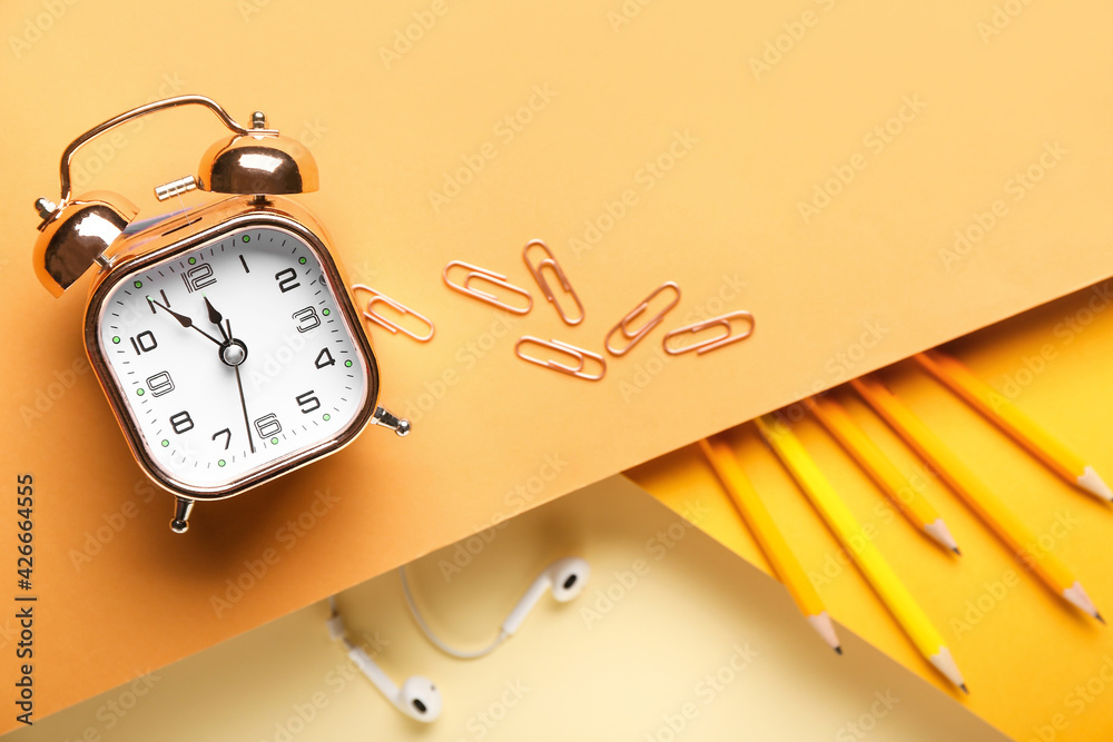 Composition with alarm clock, earphones and stationery on color background