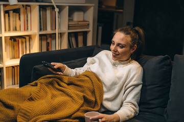 Wall Mural - young woman relaxing on couch and watching television at her home