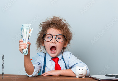 Cute kid girl holding dollars and have an idea how earning much money in crisis. Serious child teaching in eyeglasses. Funny happy child face. Financial education