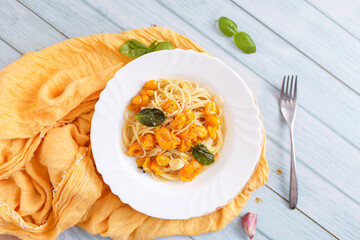 Pasta, spaghetti with yellow tomato in white plate. Blue background. Top view. Close up.