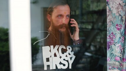 Poster - A bearded man uses the phone near the window. He holds the device near his ear, uses the mobile Internet, sending a voice message.