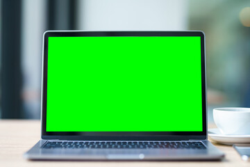 Mockup of laptop computer with empty screen with coffee cup and smartphone on table of the coffee shop background,Green screen
