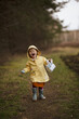 Lovely funny Dutch baby girl in a yellow waterproof coat and boots playing in the countryside field