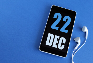 Desember 22. 22 st day of the month, calendar date. Smartphone and white headphones on a blue background. Place for your text. Winter month, day of the year concept.