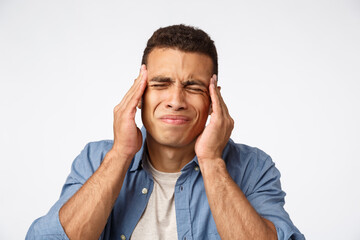 Man having huge hangover after new year party, frowning, grimacing bothered. Handsome guy suffering headache, close eyes, touching temples, have bad migraine, standing white background