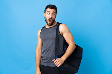 Wall Mural - Young sport man with sport bag isolated on blue background doing surprise gesture while looking to the side