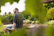 © Martin Barraud/Caia Image - Happy man taking. break from gardening on bench in summer garden