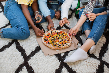 Wall Mural - Close up of four diverse friends sharing one delicious pizza during party on open terrace. Young people having tasty snack while relaxing together on weekends.