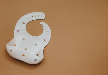 Cute baby bib for food on brown light background, top view, copy space