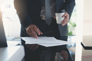 Wall Mural - Businessman reading before signing business contract with a pen and holding cup of coffee at modern office