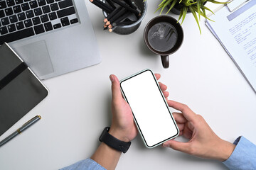 Businessman holding mobile phone with blank screen at white office desk.