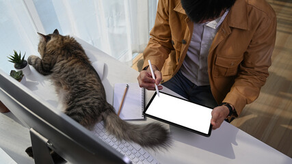 Wall Mural - Young man sitting with his lovely cat and working on digital tablet at home office.